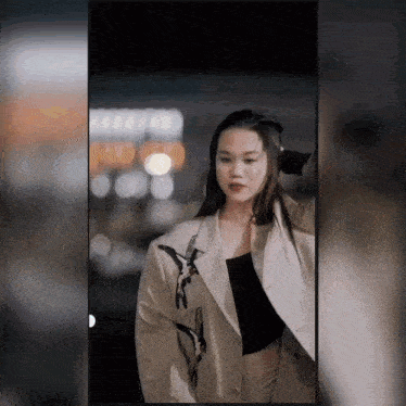 a woman wearing a blazer and a black top stands in front of a blurry background