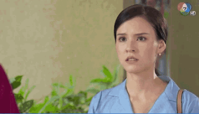 a woman in a blue shirt is making a funny face while standing in front of a wall .