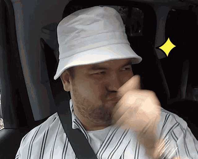 a man wearing a white hat and a striped shirt holds his nose