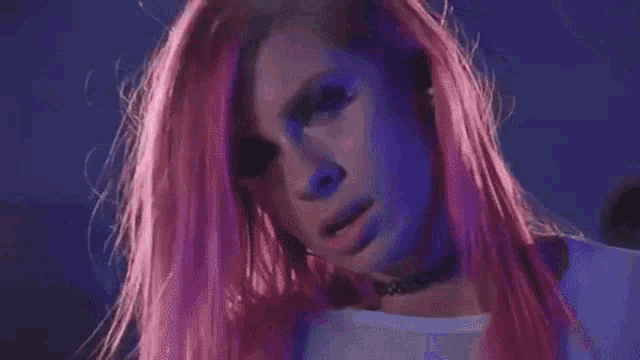a woman with pink hair and a choker on her neck is looking at the camera .