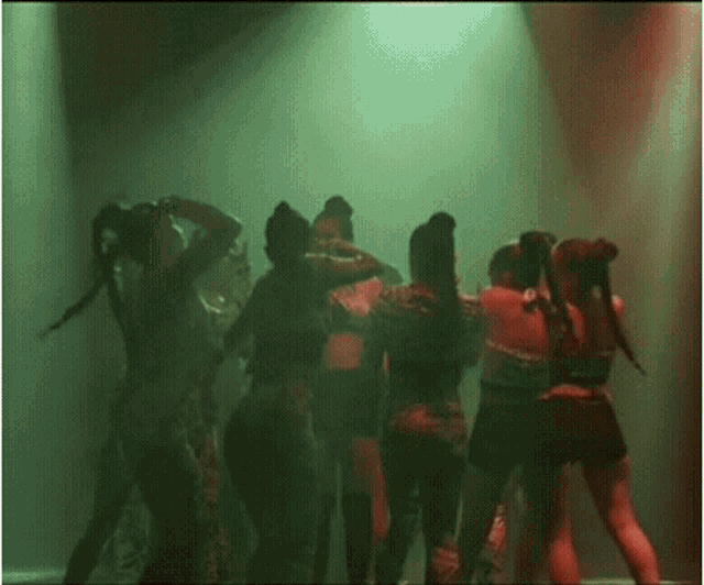 a group of women are dancing on a stage in a dark room with green lights .