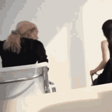 a woman is sitting in a chair in front of a mirror while another woman is standing next to her .