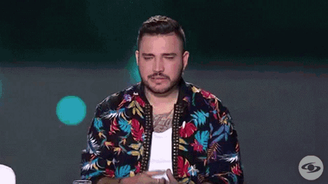 a man with a beard is sitting at a table with his eyes closed and wearing a floral shirt .