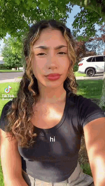 a woman with curly hair is sitting under a tree in a park .