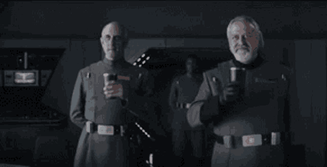 two men in military uniforms are standing next to each other in a dark room drinking beer .