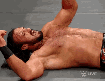 a shirtless wrestler is laying on a mat with a w live advertisement above him
