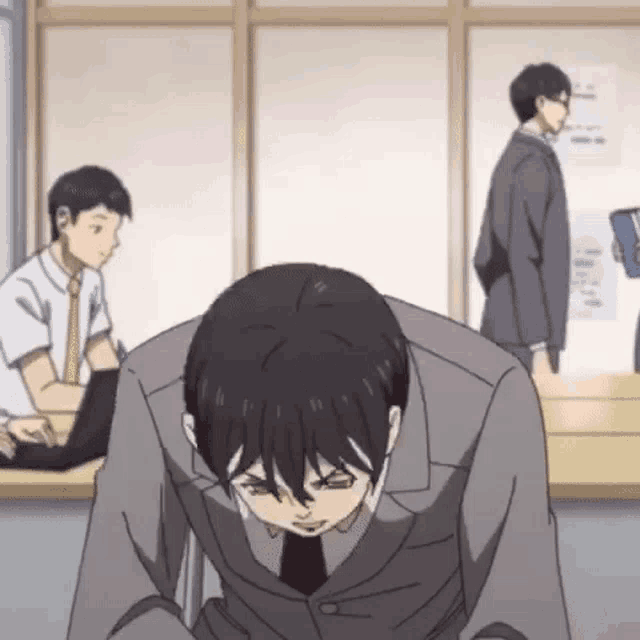 a man in a suit and tie is sitting down with his head down in a room with other men .