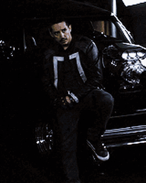 a man in a black leather jacket is standing in front of a black car