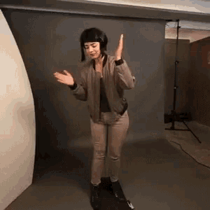 a woman in a bomber jacket and khaki pants is standing on a skateboard in a room .