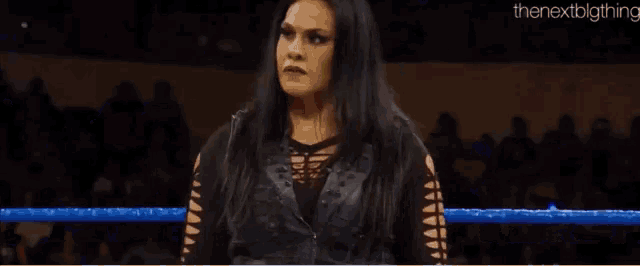 a woman is standing in a wrestling ring with a crowd watching .