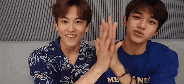 two young men are giving each other a high five while standing next to each other .