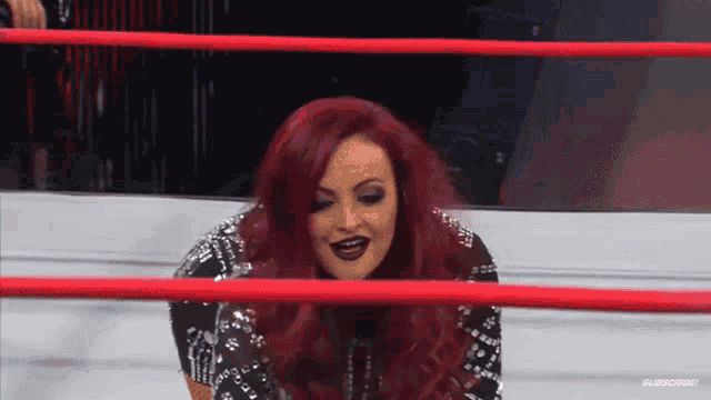 a woman with red hair is standing in a wrestling ring with a red rope .