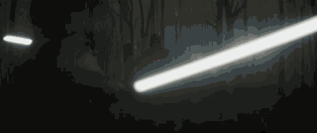 a person is holding a light saber in a dark room and a light is coming out of it .