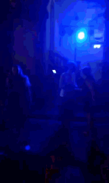 a group of people are dancing in a dark room with blue lights behind them