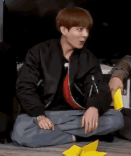 a young man is sitting on the floor with his legs crossed and holding a yellow object .