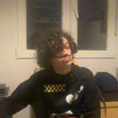a person with curly hair is wearing a black sweater with a yellow x on it .