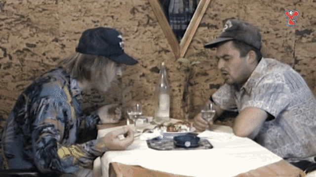two men sitting at a table with a bottle of water and a plate of food