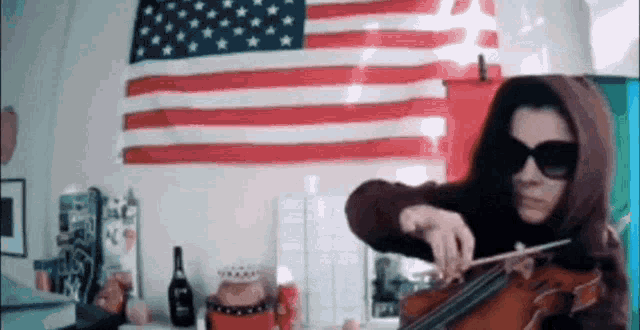 a woman in a hoodie is playing a violin in front of an american flag .