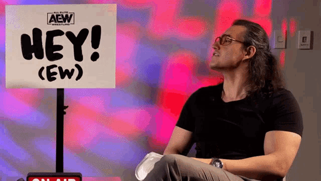 a man is sitting in front of a sign that says hey ( ew )