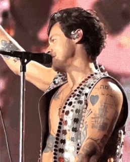 a man is singing into a microphone while wearing a sequined vest .