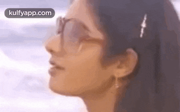 a close up of a woman wearing sunglasses and earrings on a beach .