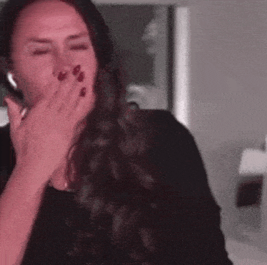 a woman is covering her mouth with her hands while wearing headphones .