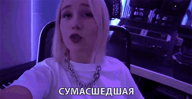 a woman in a white t-shirt is taking a selfie in front of a purple background with russian writing