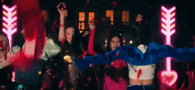 a group of women are dancing in front of a neon sign that says arrow