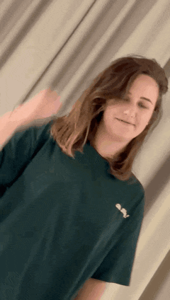 a woman wearing a green t-shirt with a white logo on the front is standing in front of a curtain