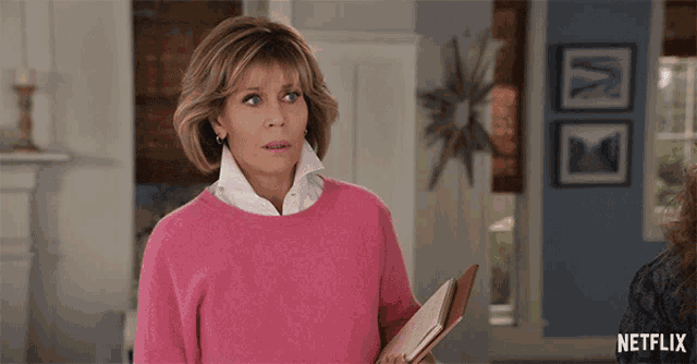 a woman in a pink sweater is holding a book and a netflix logo is visible in the corner