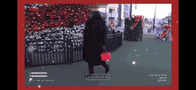 a video of a woman walking with a red purse in front of a christmas tree