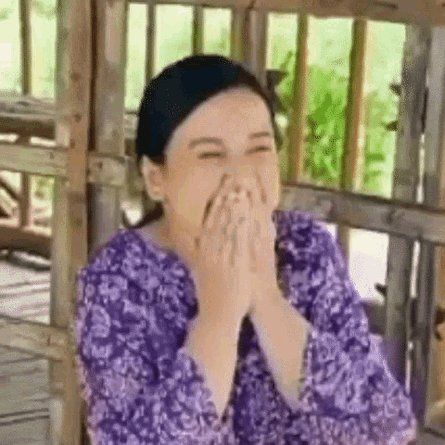 a woman in a purple shirt is laughing with her hands on her face .