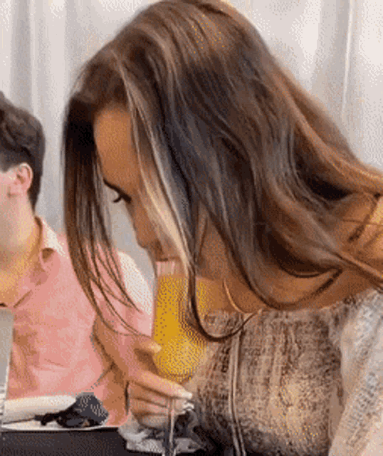 a woman drinking a glass of orange juice while sitting at a table