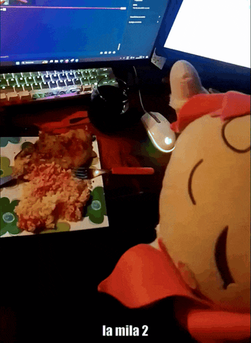a stuffed animal is sitting in front of a computer and a plate of food with the words la mila 2 on the bottom
