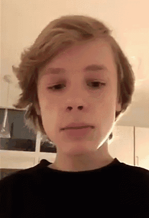 a young boy with short blonde hair is looking at the camera .