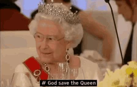 queen elizabeth ii wearing a tiara and glasses is sitting at a table with wine glasses .