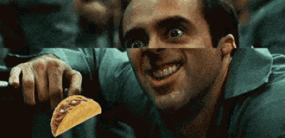 a man is smiling and holding a taco in front of his face