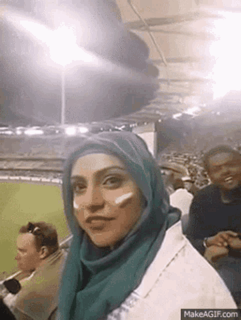 a woman wearing a hijab is taking a selfie in a stadium
