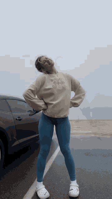 a woman wearing a sweatshirt that says " i 'm a girl " stands in front of a car