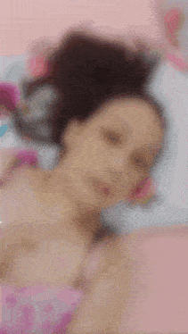 a blurry picture of a girl laying on a bed with a pink background