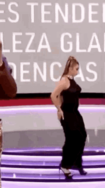 a woman in a black dress is dancing on a stage in front of a large screen .