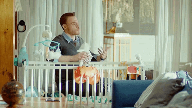 a man is sitting in a crib holding a baby in his hands
