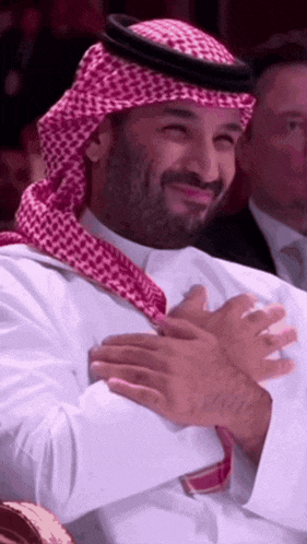 a man wearing a head scarf and a white shirt is smiling and clapping his hands