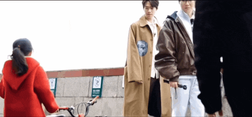 a woman in a red hoodie is holding a bicycle in front of two men