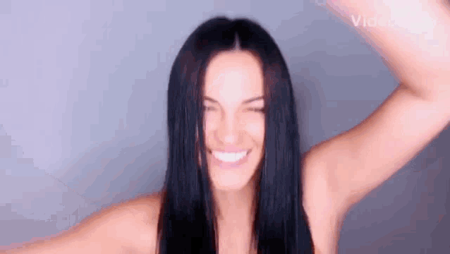 a woman with long black hair is smiling and making a funny face with her hands in the air .