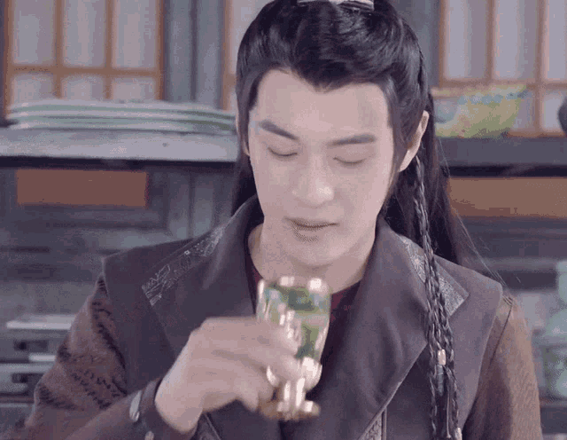 a man with long hair is drinking from a cup with a green liquid in it