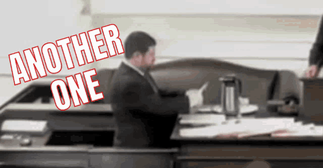 a man in a suit sits at a table with the words another one written on the top