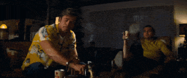 two men are sitting in chairs in a living room and one of them is holding a can of beer