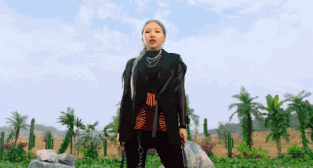 a woman in a black jacket stands in front of a field of palm trees