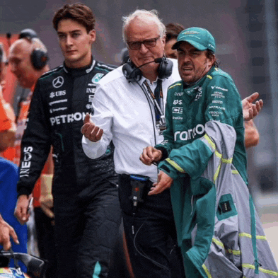 a man in a green petronas jacket talks to another man in a white shirt